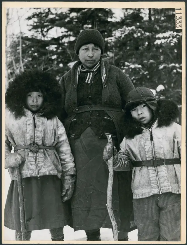 A woman and two children in buckskin parkas trimmed with bear fur